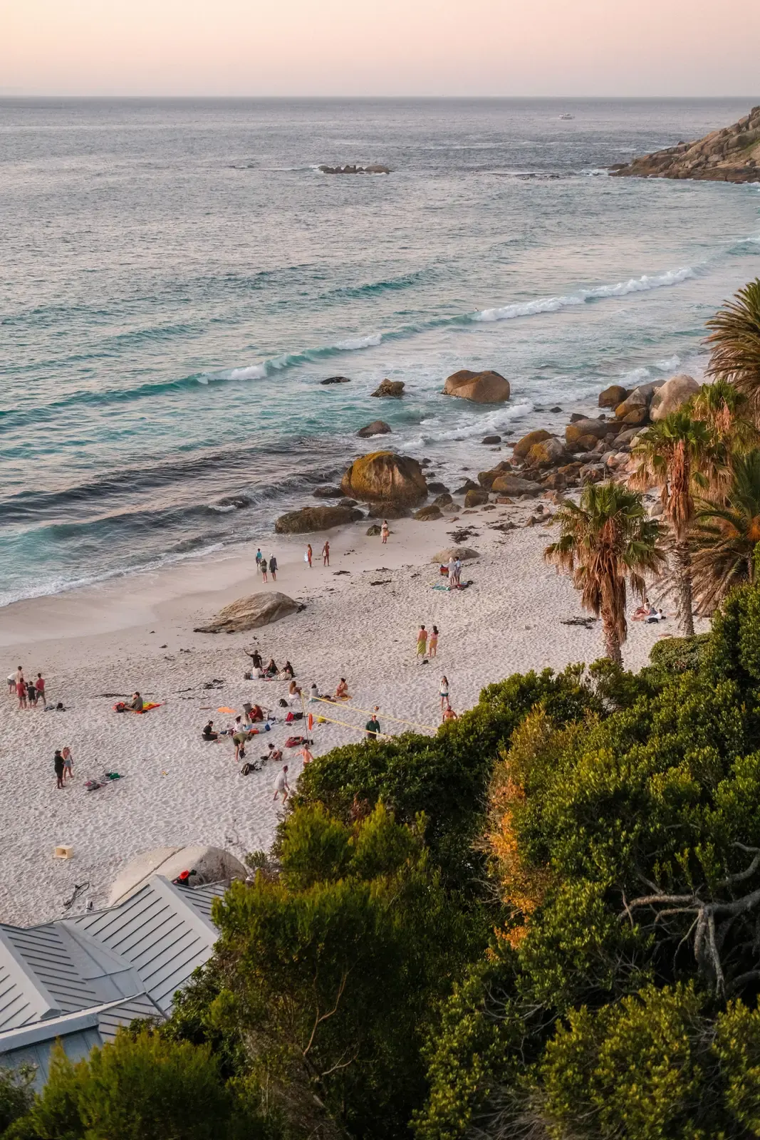 A sheltered Cape Town beach with granite boulders and palms in warm evening light