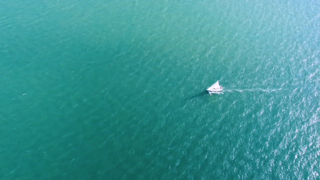 A distant sailing boat on turquoise water; general sailing inspiration, no named destination.